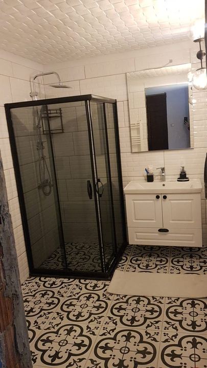 Desenli zemin karosu, siyah çerçeveli duşakabin ve beyaz lavabo dolabı