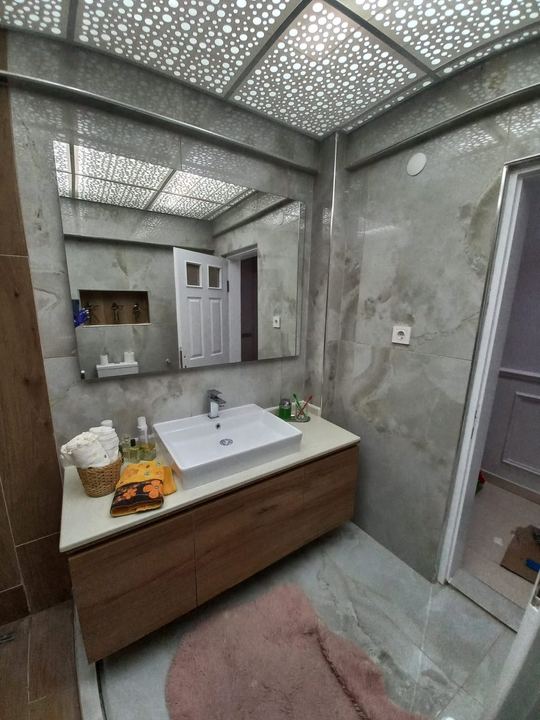 Mermer görünümlü fayanslı banyo, ahşap lavabo dolabı ve geniş ayna